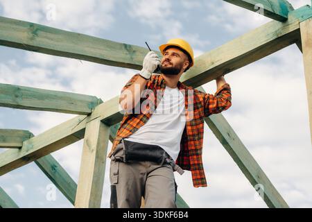 Giving orders by using walkie talkie. Construction worker is on the roof of a house. Stock Photo