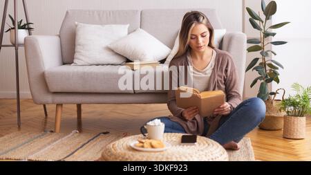 Young woman reading book, sitting on floor at home Stock Photo