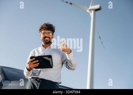 Smiling, positive facial expression. Male engineer in field checking on wind turbine production. Stock Photo