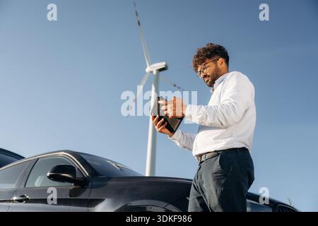 Side view, holding digital tablet. Male engineer in field checking on wind turbine production. Stock Photo