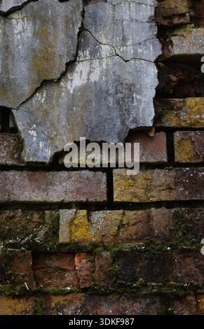 A cracked and crumbling brick wall with moss and lichen. Stock Photo