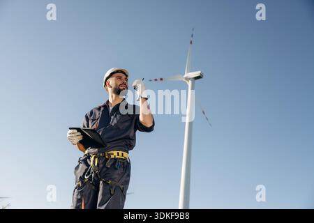 Using walkie talkie. Engineer in field checking on wind turbine production. Stock Photo