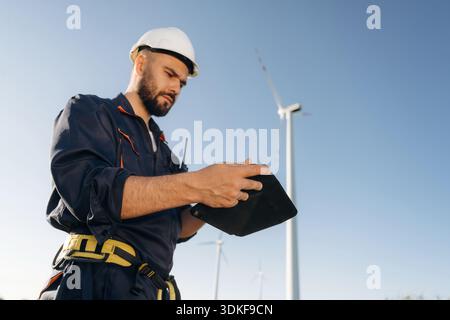 Reading information on digital tablet. Engineer in field checking on wind turbine production. Stock Photo