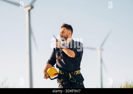 Technician is giving orders by walkie talkie. Engineer in field checking on wind turbine production. Stock Photo