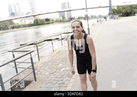 AuthentiCITY, sportive laughter during a rest between athlete's outdoor exercises, laughing jogger taking a funny break, mid adult woman training at r Stock Photo