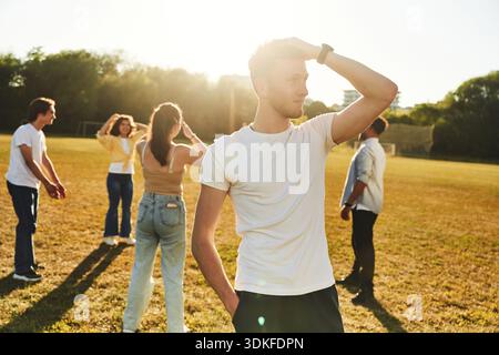 Bright sunlight, guy is standing and posing. Young friends are having fun on the field. Stock Photo
