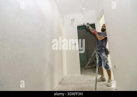 Construction worker applies a white coat, putty on the wall, using nozzle, plastering and skim coating walls spraying mixture under pressure Stock Photo
