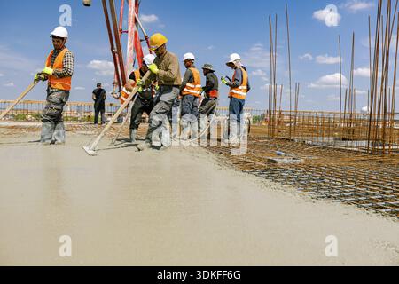 Team of construction workers are pouring and leveling fresh concrete using handmade tool over rectangular armature Stock Photo