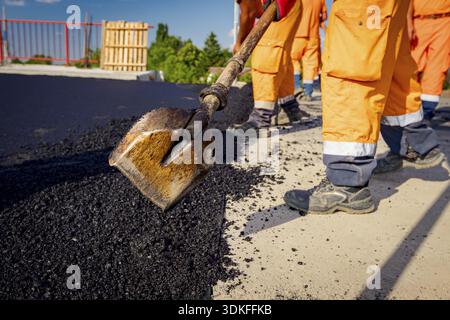 Few workers are using shovels to level, set up layer of fresh tarmac to right measures, pouring hot asphalt Stock Photo