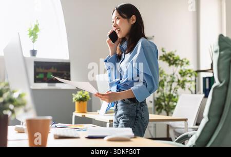 Lady holding paper reading report talking on phone at office Stock Photo