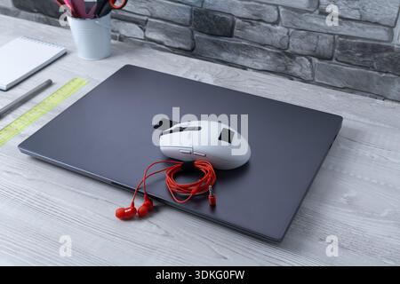 Workspace with laptop, mouse, and headphones on desk during daytime in a home office setting Stock Photo
