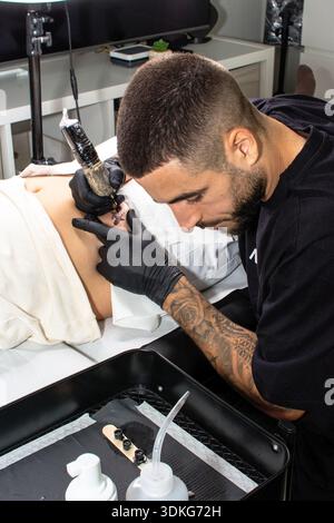 Tattoo artist creating body art on client's abdomen Stock Photo