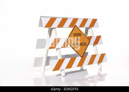 Orange and white striped road construction barrier with Work in Progress sign over white background Stock Photo