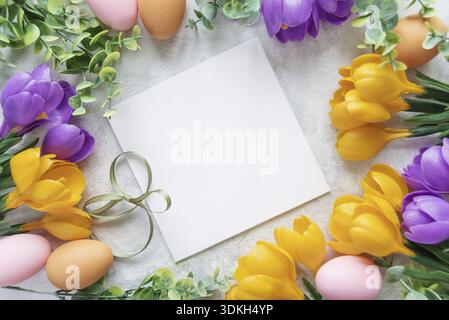 Easter card with blank white sheet surrounded by frame of yellow and purple crocus flowers and colorful Easter eggs Stock Photo