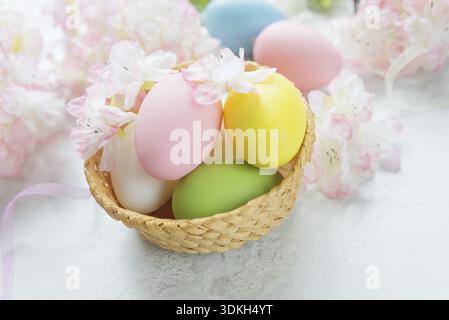 Easter composition with multicolored easter eggs in a wicker basket on the background of delicate pink flowers of the cherry blossoms Stock Photo