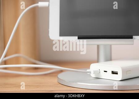 Tablet computer charging from power bank on shelf in room, closeup Stock Photo
