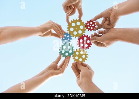 Many hands with colorful gears against sky, bottom view Stock Photo