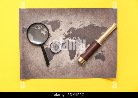 Composition with modern compass, world map and magnifier on yellow background Stock Photo