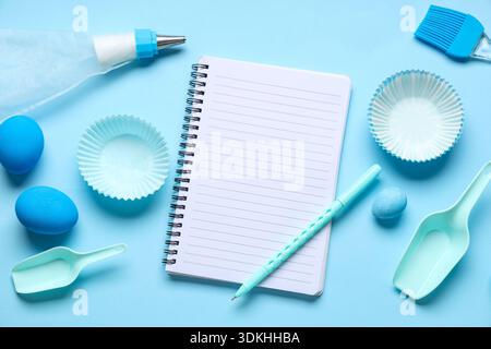 Blank notepad for recipes with pen, baking tools and Easter eggs on blue background Stock Photo