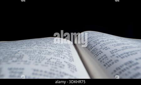 Open book with pages displaying text, placed on a dark surface, close view captures printed words and layout clearly Stock Photo