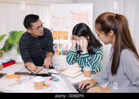A tense business meeting where a team discusses design problems and project challenges. The man tries to explain solutions while one team member looks Stock Photo