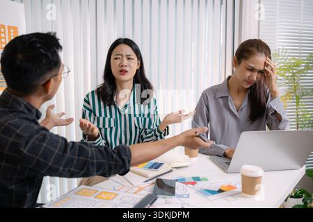 A tense business meeting where a team discusses design problems and project challenges. The man tries to explain solutions while one team member looks Stock Photo