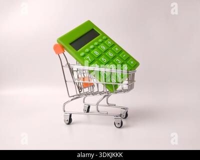Miniature shopping cart holding a small, bright green calculator. Stock Photo