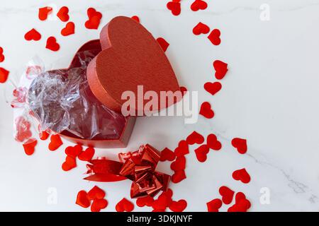 Top-view of an open red heart gift box with ribbon bow and scattered red heart confetti on marble, copy space right Stock Photo