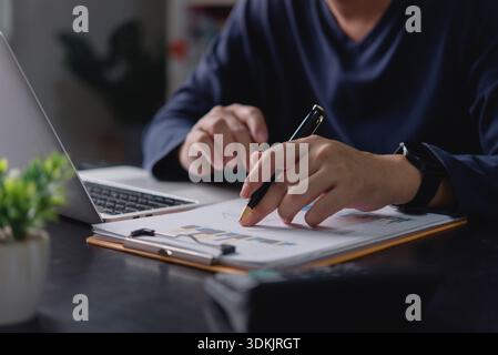 Businessman analyzing financial data report, hand with pen pointing at chart. Man working with laptop office desk, reviewing business performance, inv Stock Photo