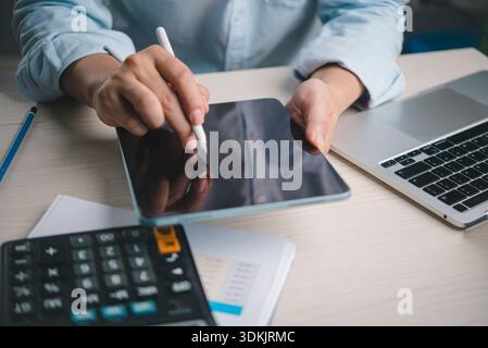 Professional uses stylus on tablet beside laptop calculator documents at office desk for digital note taking esignature planning accounting productivi Stock Photo