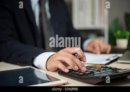 Accountant works on numbers using calculator near paperwork and laptop in office for invoice billing audit tax preparation financial analysis accuracy Stock Photo