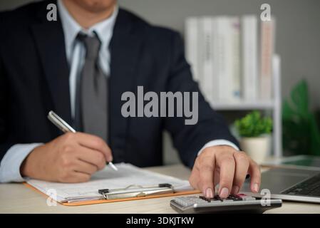 Financial planning, Professional businessman calculates numbers on calculator while working with laptop and papers, analyzing budget, audit, and accou Stock Photo
