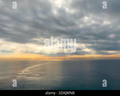 Dramatic cloudy sky over calm sea during golden sunset hour Stock Photo