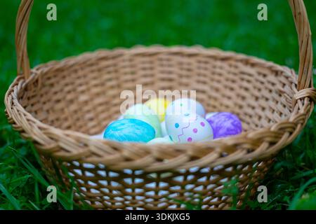 Decorated colorful easter eggs are lying in wicker basket on green grass Stock Photo