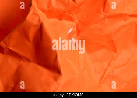 Bright orange textured paper exhibits intricate folds and creases, evoking creativity. Stock Photo