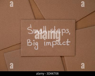 Cardboard with handwritten words Small Steps, Big Impact on a cardboard pieces background. Stock Photo