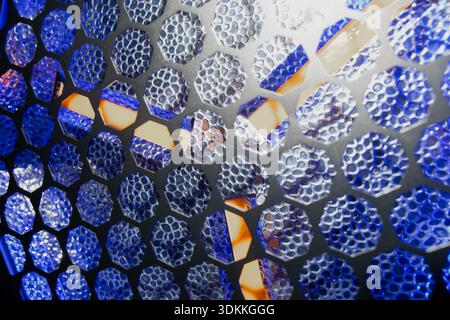 Abstract macro of perforated metal mesh with hexagon honeycomb pattern, blue and silver reflective texture, warm orange highlights, and high contrast Stock Photo