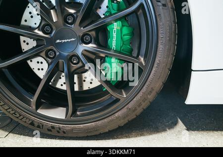 Closeup of green brake caliper, wheel on black alloy rim with drilled rotor and low profile tire, white coupe Porsche, Warsaw, Poland 24-06-2025 Stock Photo