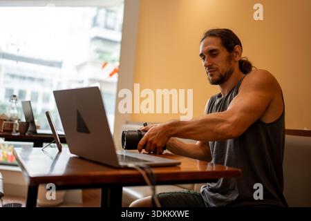 Man holding camera lens and working on laptop at a cafe workspace Stock Photo