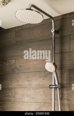This shows a shower head mounted on a wall with a handheld shower option. The background features wooden wall panels, creating a clean and simple desi Stock Photo