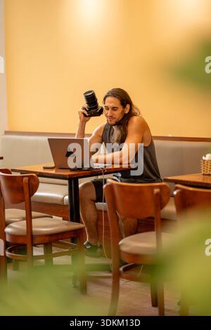 Male photographer working on laptop holding camera in cafe Stock Photo