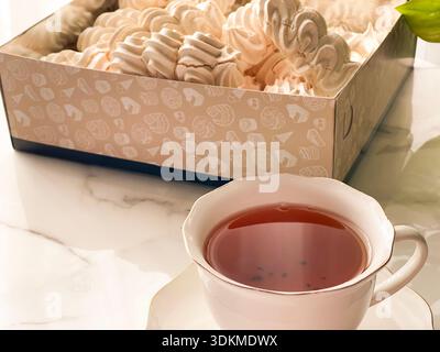 Tea with Zephyr Marshmallows. Cozy tea time with a cup of hot black tea and soft airy Russian zephyr marshmallows on a light table near the window. Stock Photo