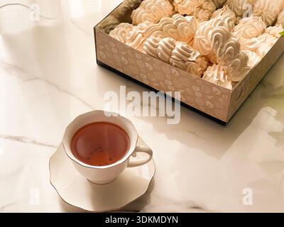 Tea with Zephyr Marshmallows. Cozy tea time with a cup of hot black tea and soft airy Russian zephyr marshmallows on a light table near the window. Stock Photo