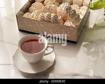 Tea with Zephyr Marshmallows. Cozy tea time with a cup of hot black tea and soft airy Russian zephyr marshmallows on a light table near the window. Stock Photo