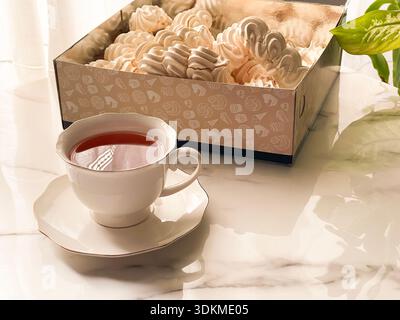 Tea with Zephyr Marshmallows. Cozy tea time with a cup of hot black tea and soft airy Russian zephyr marshmallows on a light table near the window. Stock Photo