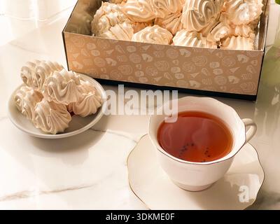 Tea with Zephyr Marshmallows. Cozy tea time with a cup of hot black tea and soft airy Russian zephyr marshmallows on a light table near the window. Stock Photo