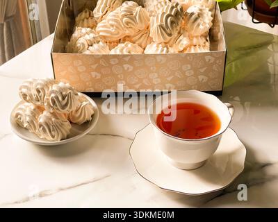 Tea with Zephyr Marshmallows. Cozy tea time with a cup of hot black tea and soft airy Russian zephyr marshmallows on a light table near the window. Stock Photo