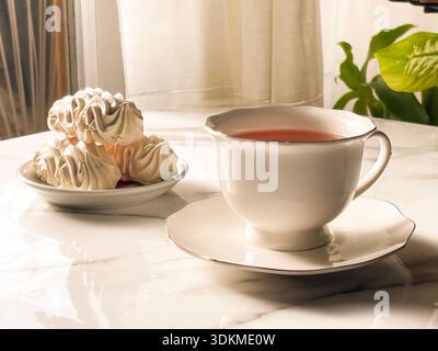 Tea with Zephyr Marshmallows. Cozy tea time with a cup of hot black tea and soft airy Russian zephyr marshmallows on a light table near the window. Stock Photo