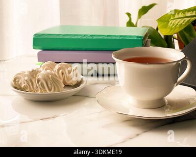 Tea with Zephyr Marshmallows. Cozy tea time with a cup of hot black tea and soft airy Russian zephyr marshmallows on a light table near the window. Stock Photo