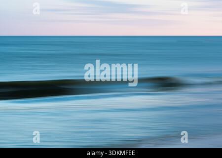 Gentle waves appear as soft motion blur in the fading twilight over the sea. Stock Photo